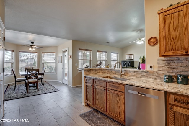 kitchen featuring decorative backsplash, stainless steel dishwasher, brown cabinetry, a sink, and a peninsula