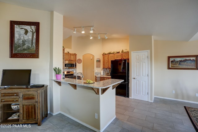 kitchen featuring arched walkways, lofted ceiling, appliances with stainless steel finishes, a breakfast bar, and a peninsula