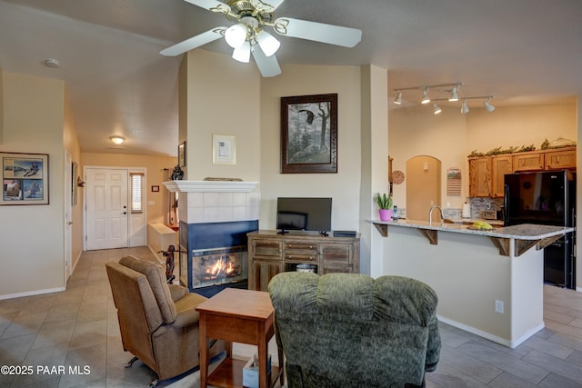 living area featuring arched walkways, a tiled fireplace, ceiling fan, vaulted ceiling, and light tile patterned flooring