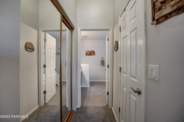 corridor featuring light carpet, light tile patterned floors, visible vents, baseboards, and a textured wall