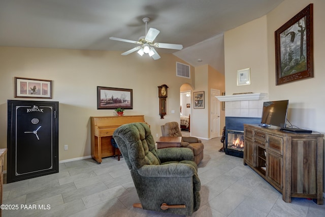 living area with arched walkways, lofted ceiling, visible vents, a tiled fireplace, and ceiling fan