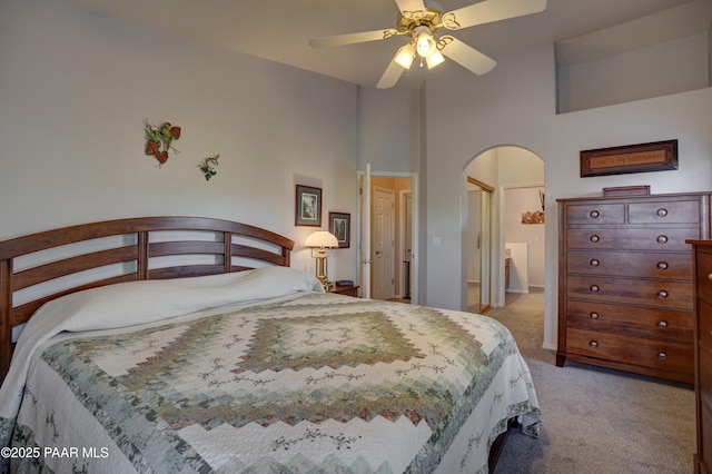 bedroom featuring light carpet, ceiling fan, a high ceiling, and arched walkways