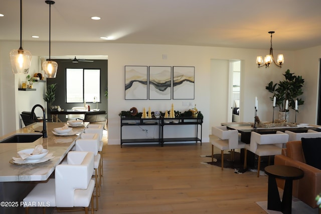 dining space with ceiling fan with notable chandelier, wood-type flooring, and sink