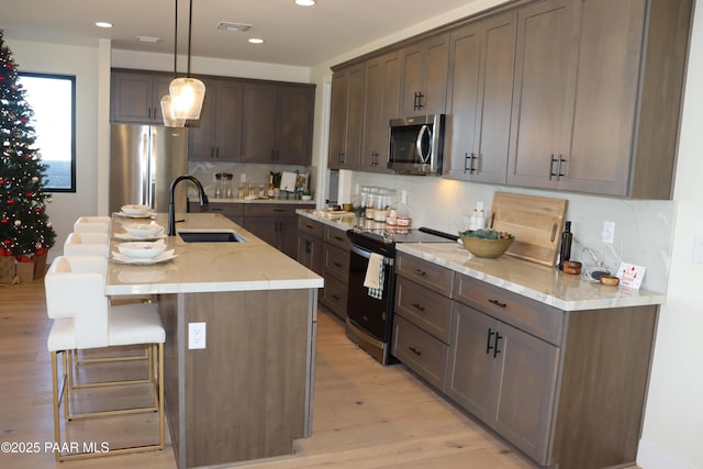 kitchen with sink, light stone countertops, an island with sink, decorative light fixtures, and stainless steel appliances