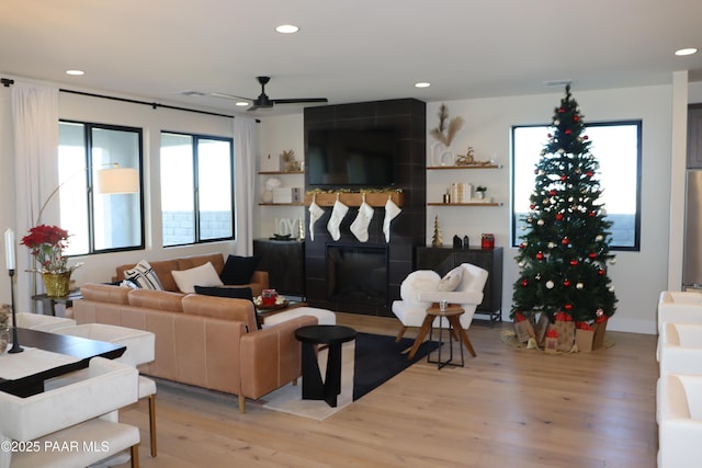 living room featuring a tile fireplace, ceiling fan, and light hardwood / wood-style floors