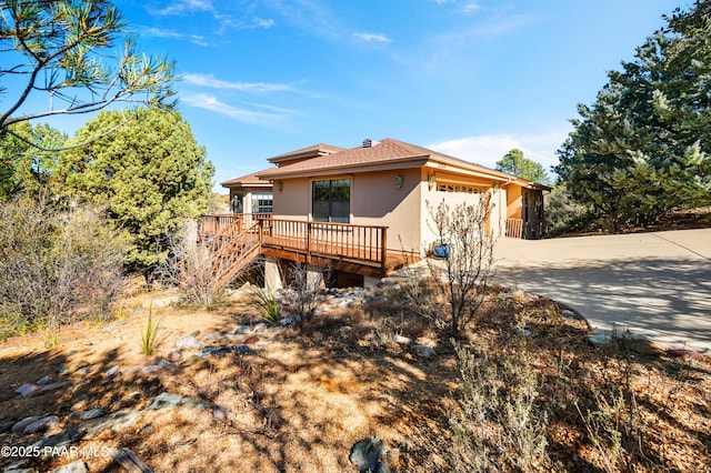 view of front of home featuring a deck, an attached garage, stairs, driveway, and stucco siding