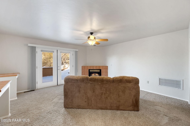 living room featuring a tiled fireplace, light colored carpet, french doors, and ceiling fan