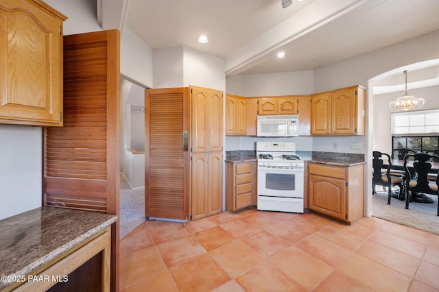 kitchen featuring white appliances, hanging light fixtures, light carpet, dark stone counters, and a chandelier