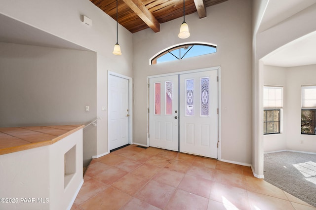 carpeted entryway featuring wood ceiling, a high ceiling, and beamed ceiling