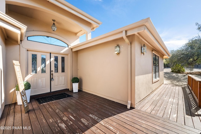 view of exterior entry featuring a wooden deck and stucco siding