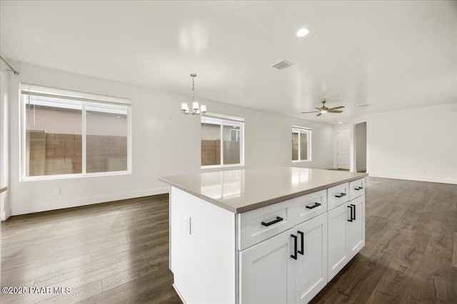 kitchen featuring white cabinetry, a center island, hanging light fixtures, dark hardwood / wood-style flooring, and ceiling fan with notable chandelier