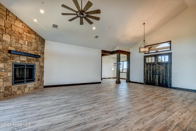 unfurnished living room with a fireplace, ceiling fan with notable chandelier, light hardwood / wood-style floors, and high vaulted ceiling