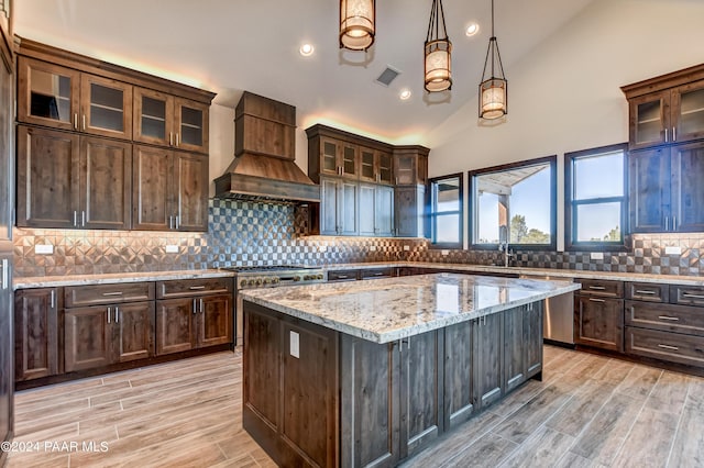 kitchen featuring custom exhaust hood, lofted ceiling, decorative backsplash, light stone countertops, and decorative light fixtures