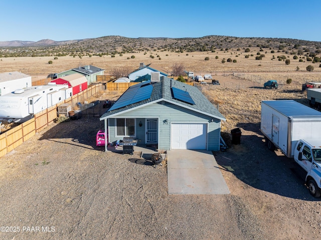 view of front of property featuring an attached garage, a mountain view, fence, concrete driveway, and roof mounted solar panels