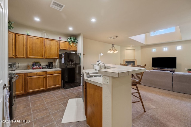 1222 Crown Ridge Dr, Prescott, AZ 86301 - kitchen with a skylight, freestanding refrigerator, a kitchen breakfast bar, brown cabinetry, and a glass covered fireplace