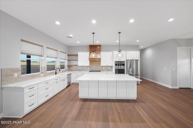 kitchen with backsplash, stainless steel appliances, decorative light fixtures, light hardwood / wood-style flooring, and a center island