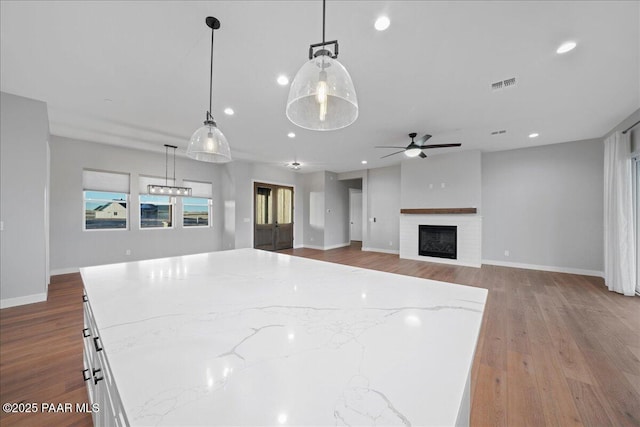 kitchen featuring pendant lighting, white cabinets, light stone countertops, and light hardwood / wood-style flooring