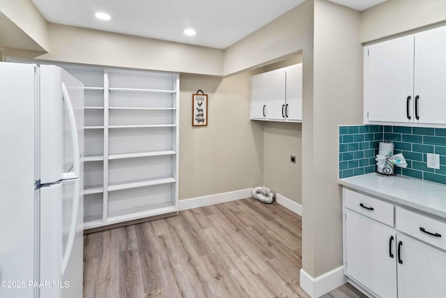 laundry area with electric dryer hookup, light hardwood / wood-style flooring, and cabinets