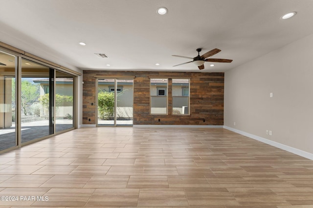 unfurnished room featuring plenty of natural light, wooden walls, and ceiling fan