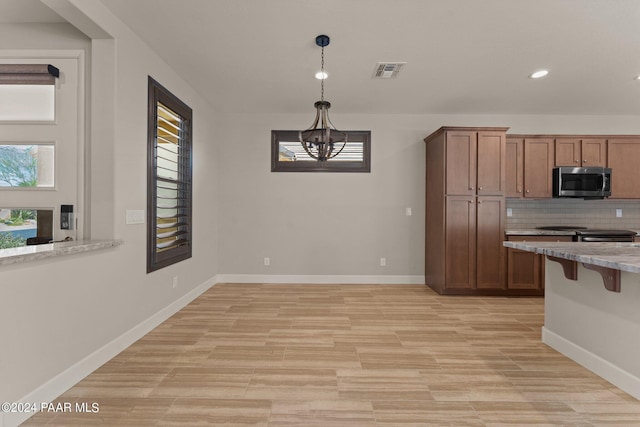 kitchen featuring tasteful backsplash, a notable chandelier, light hardwood / wood-style floors, pendant lighting, and a breakfast bar area