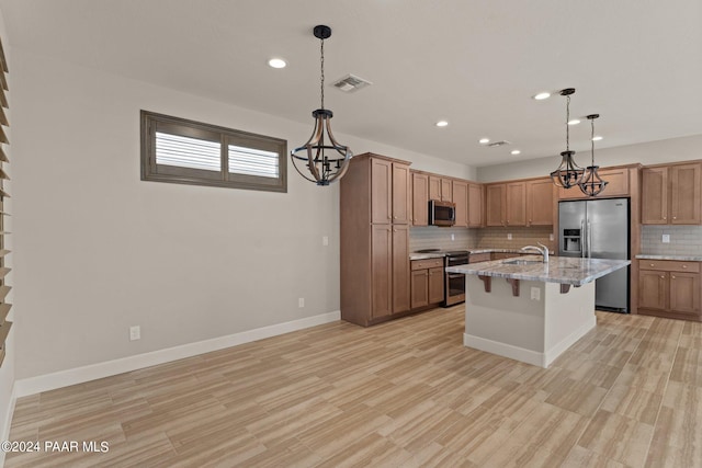 kitchen with a breakfast bar, stainless steel appliances, sink, a center island with sink, and light hardwood / wood-style floors