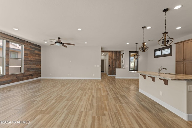 unfurnished living room with ceiling fan, sink, wooden walls, and light hardwood / wood-style flooring