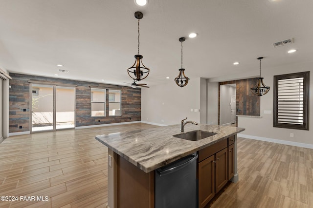 kitchen with light stone countertops, a kitchen island with sink, sink, decorative light fixtures, and dishwasher