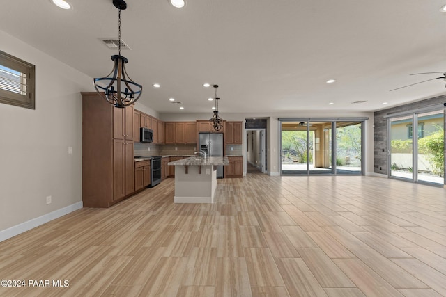 kitchen featuring pendant lighting, a kitchen island with sink, light hardwood / wood-style flooring, appliances with stainless steel finishes, and light stone counters