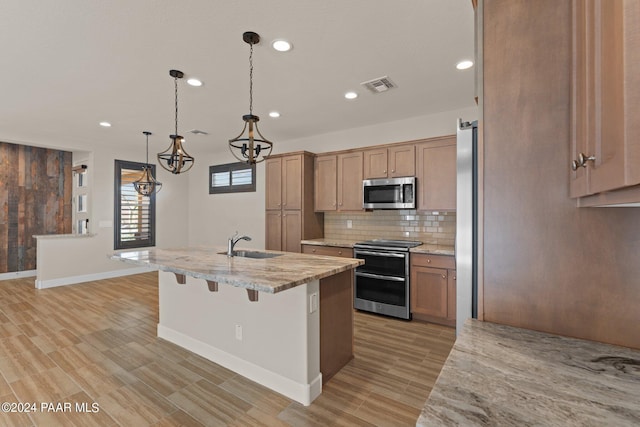 kitchen with light stone countertops, light wood-type flooring, stainless steel appliances, sink, and decorative light fixtures