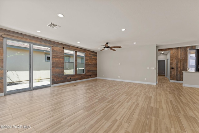 unfurnished living room with light hardwood / wood-style flooring, ceiling fan, and wood walls