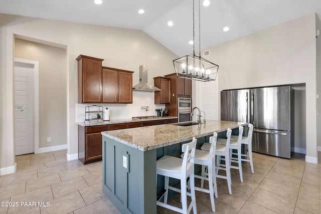 kitchen featuring wall chimney range hood, light tile patterned floors, a sink, lofted ceiling, and stainless steel appliances