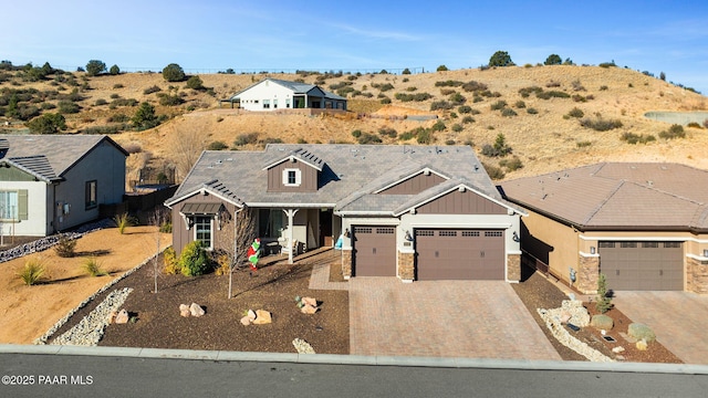 view of front of house featuring board and batten siding, decorative driveway, an attached garage, and stone siding