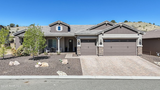 craftsman-style home with an attached garage, a porch, decorative driveway, and stone siding