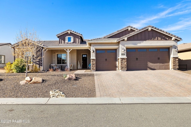 craftsman-style home with stone siding, decorative driveway, stucco siding, an attached garage, and a tile roof