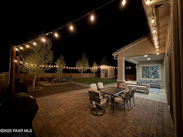 patio at night with an outdoor hangout area, a storage shed, a fenced backyard, an outbuilding, and outdoor dining area