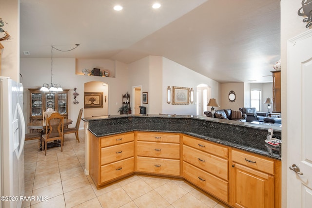 kitchen featuring open floor plan, vaulted ceiling, light tile patterned floors, dark stone countertops, and white fridge with ice dispenser