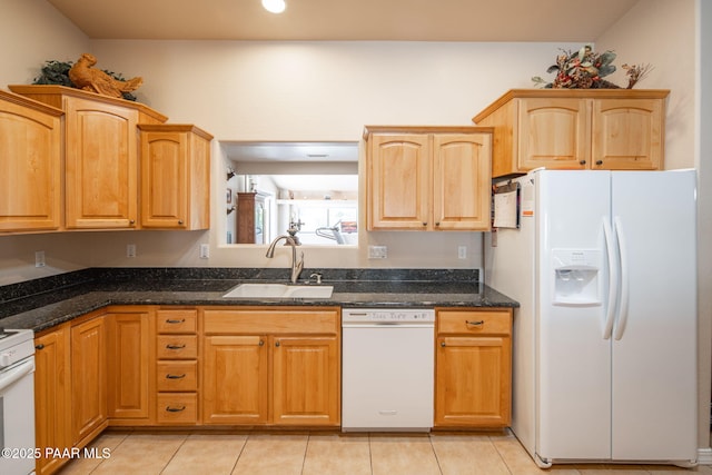 kitchen featuring white appliances, dark stone counters, light tile patterned floors, and a sink