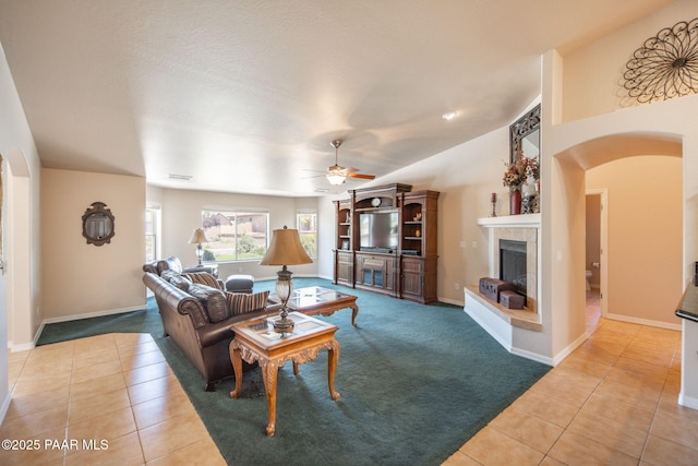 carpeted living room featuring arched walkways, tile patterned flooring, a tiled fireplace, and a ceiling fan