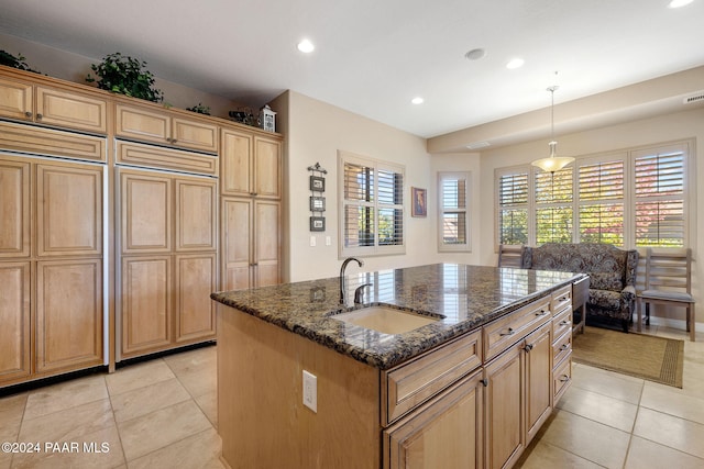 kitchen with dark stone counters, sink, light tile patterned floors, a center island with sink, and hanging light fixtures