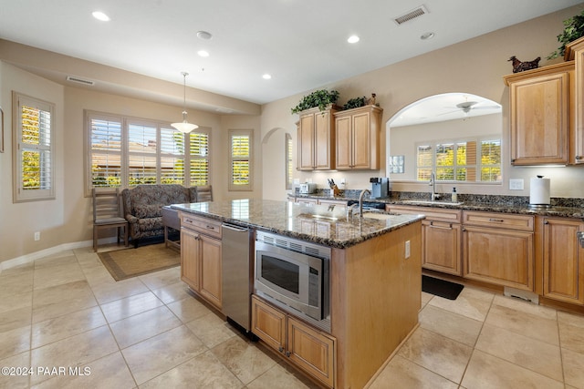 kitchen featuring a center island, stainless steel microwave, ceiling fan, dark stone countertops, and decorative light fixtures