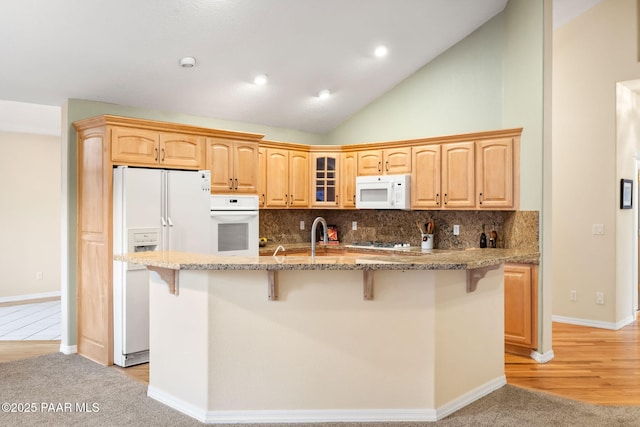 kitchen with lofted ceiling, white appliances, a breakfast bar, tasteful backsplash, and a center island with sink