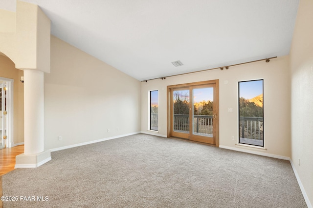 carpeted empty room with vaulted ceiling and decorative columns