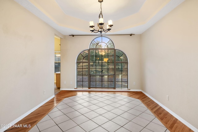 spare room with a raised ceiling, a chandelier, and light hardwood / wood-style floors