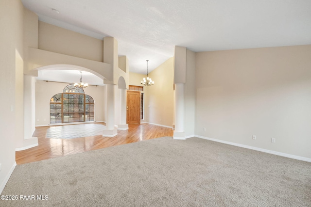 unfurnished living room featuring an inviting chandelier, high vaulted ceiling, and light carpet