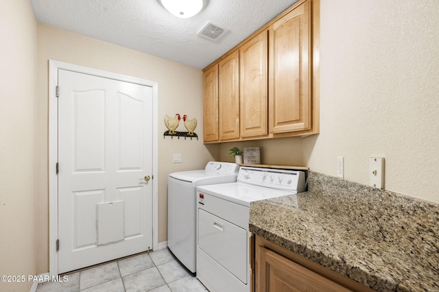 clothes washing area featuring cabinets, washing machine and dryer, light tile patterned floors, and a textured ceiling