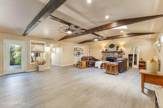 living room with vaulted ceiling with beams, light hardwood / wood-style floors, a stone fireplace, and ceiling fan