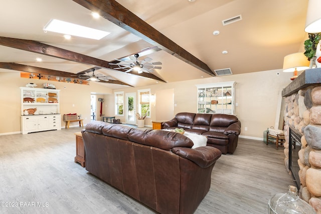 living room featuring lofted ceiling with skylight, a fireplace, ceiling fan, and light wood-type flooring