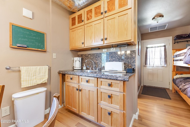 kitchen featuring light hardwood / wood-style floors, tasteful backsplash, dark stone countertops, and sink