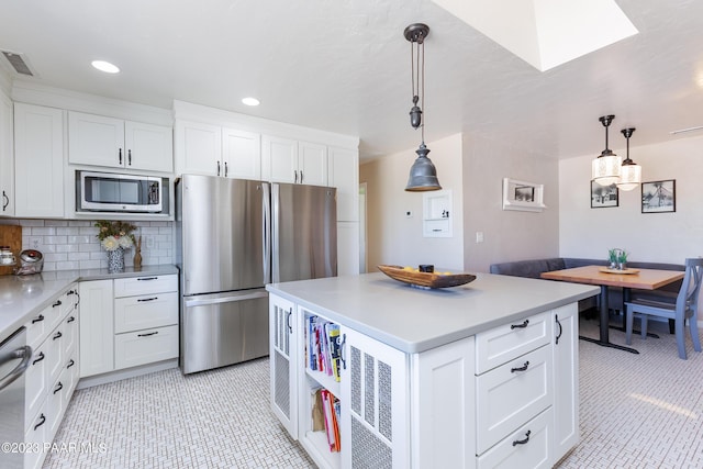 kitchen featuring a center island, white cabinets, hanging light fixtures, decorative backsplash, and appliances with stainless steel finishes