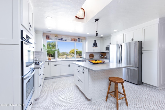 kitchen with a kitchen island, pendant lighting, a kitchen bar, white cabinets, and appliances with stainless steel finishes